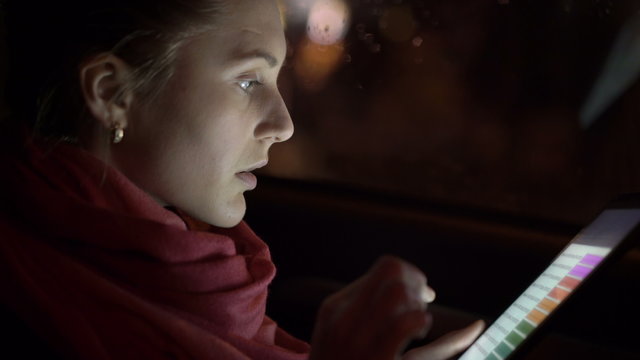 Young girl sitting in a car and using the tablet at night. 4K