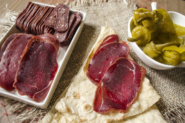 Slices dried beef coated spices on white ware and thin bread lie on sackcloth