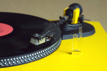 Turntable in yellow case playing a vinyl record with white label. Horizontal photo top view closeup