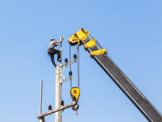 Electrician working on electricity power pole with crane.