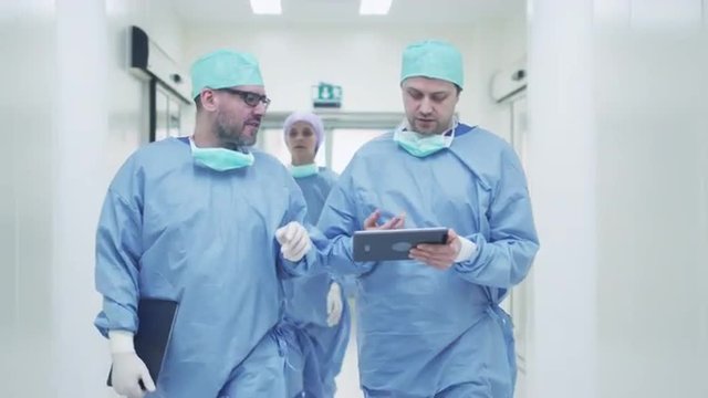 Two Doctors Walking through Hospital and Chatting. Holding Tablet in Hands. Shot on RED Cinema Camera.