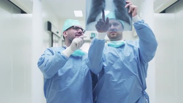 Two Doctors Walking through Hospital and Chatting. Holding Tablet in Hands. Shot on RED Cinema Camera.