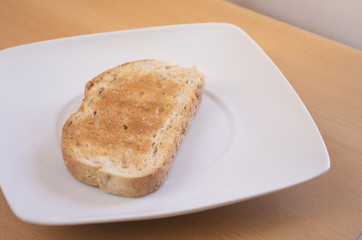 Tostada de pan en un plato blanco con luz natural encima de una mesa. Desayuno.