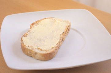 Tostada con mantequilla en un plato blanco con luz natural encima de una mesa. Desayuno.