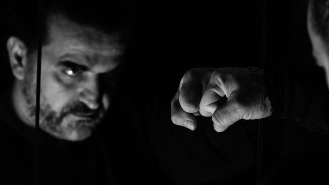Angry man fist punching mirror and his reflection, monochromatic image