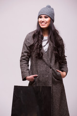 Gorgeous young brunette woman wearing in coat and hat, holding shopping bag isolated on grey...