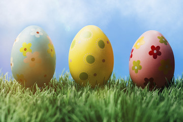 Drei bunt bemalte Ostereier im Gras vor blauem Himmel