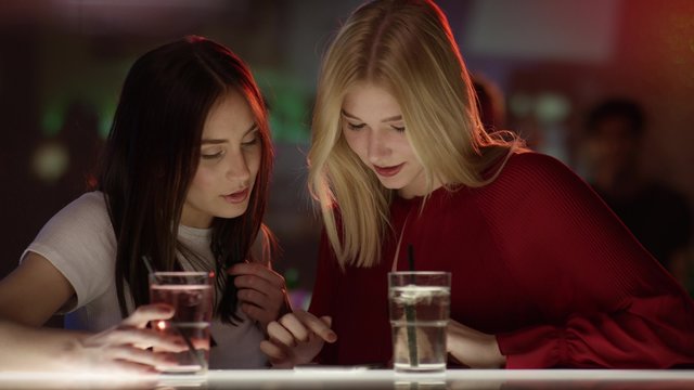 M&auml;dchen an Bar, eine tippt ins Handy
