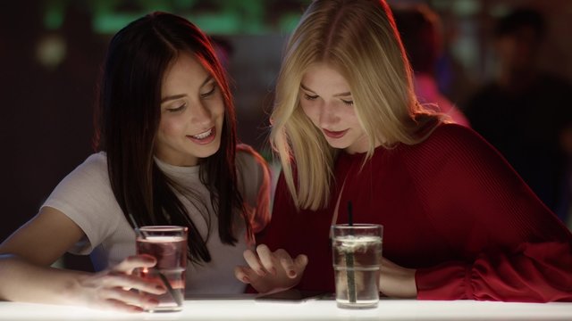 Lachende M&auml;dchen an Bar mit Handy