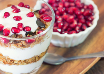 yogurt with homemade granola and pomegranate on the bright wooden board