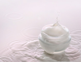 Moisturizing cosmetic  cream  stands on the pink milk background with milk splash
