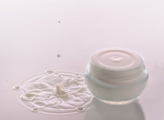 Moisturizing cosmetic  cream  stands on the pink milk background with milk splash and  falling drops