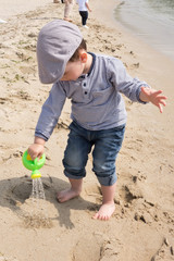 Cute little boy playing with watering can on the beach