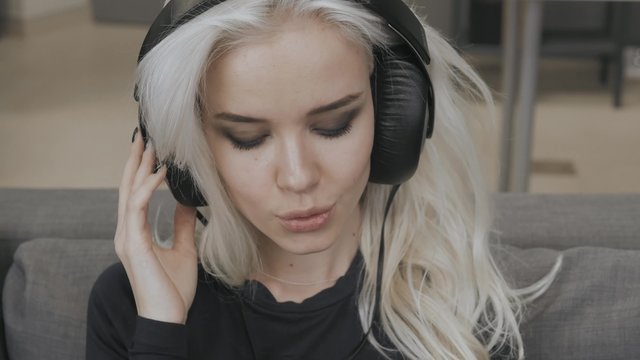 Beautiful Blonde Model Girl Listening Music with Big Headphones and Smile