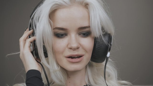 Beautiful Blonde Model Girl Listening Music with Big Headphones and Smile
