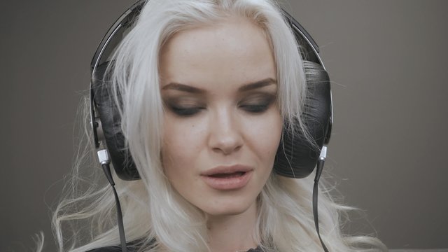 Beautiful Blonde Model Girl Listening Music with Big Headphones and Smile