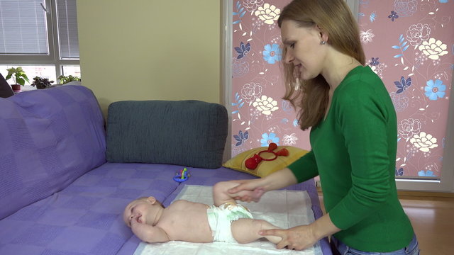 Mother exercise little baby boy son legs on bed at home. Smiling newborn. Woman care newborn health. 4K UHD video clip.
