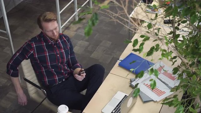 A bearded man with a smirk on her face looking to the smartphone.