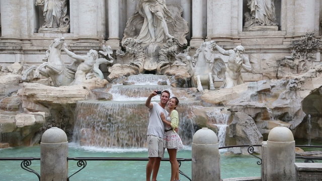 Tourist couple using smart phone on travel taking selfie photo by Trevi Fountain in Rome, Italy. Happy young romantic couple traveling in Europe taking self-portrait with smartphone camera.