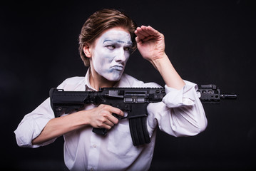 Fototapeta premium Actor in makeup mime with weapon/Male actor with mime make-up with rifle in hands looks in search of the enemy,on black background