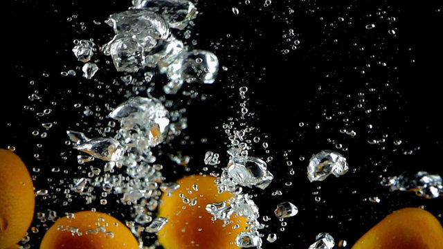 Twelve tangerines being dropped into water in super slow motion (500 frames per second) against a black background.

