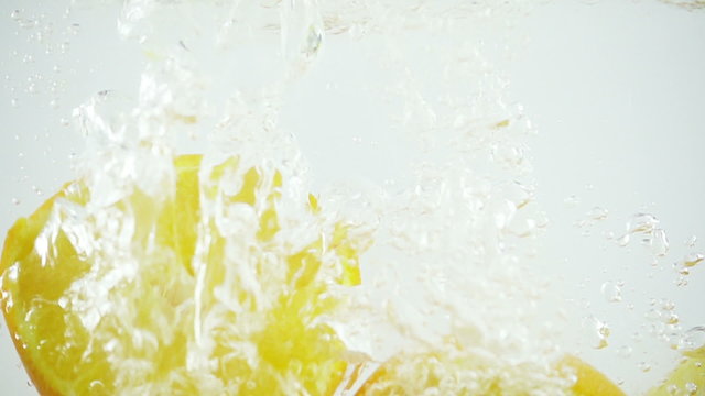 Four sectioned oranges being dropped into water in super slow motion (500 frames per second) against a white background.
