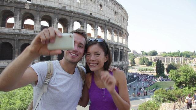 Happy travel couple taking selfie by Coliseum, Rome, Italy. Smiling young romantic couple traveling in Europe taking self portrait photo with smartphone camera in front of Colosseum. Man and woman.