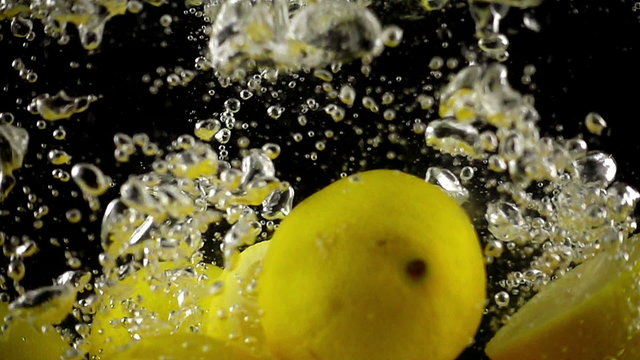 A set of whole and sectioned lemons being dropped into water in super slow motion (500 frames per second) against a black background.
