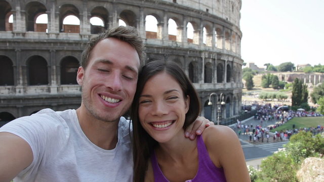 Selfie - Romantic travel couple by Coliseum, Rome, Italy. Happy lovers on honeymoon sightseeing having fun in front of Colosseum. Woman and man in tourism travel concept.