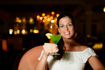 Beautiful woman at night club drinking a green cocktail and toasting. Tranquil female having fun and enjoying nightlife.