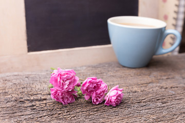 Pink rose and mug with coffee on a wooden table.