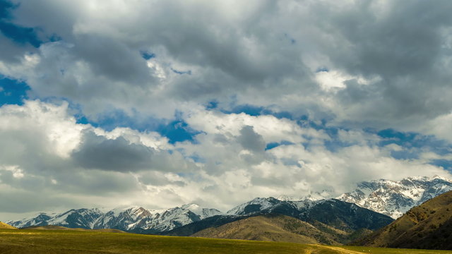 4K Timelapse. Clouds float over the autumn field with a view of snow-capped mountains