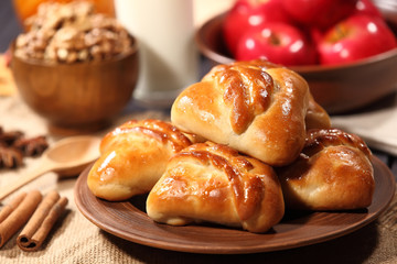 Homemade cakes are a pottery plate next to cup of nuts and a bunch of red apples on a wooden table. Selective focus