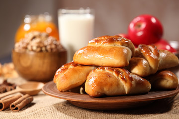 Homemade cakes are a pottery plate next to cup of nuts and a bunch of red apples on a wooden table....