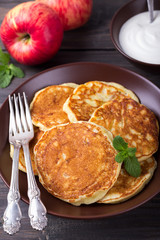 Cottage cheese pancake with apples in ceramic bowl with sour cream on a dark wooden table 