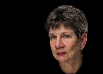 Beauty glamour portrait of senior elderly woman lady with short brown grey hair and with serious melancholy sad depressed disappointed judgmental expression isolated on black background