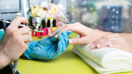 Closeup shot of a woman in a nail salon receiving a manicure by a beautician with nail file. Woman...