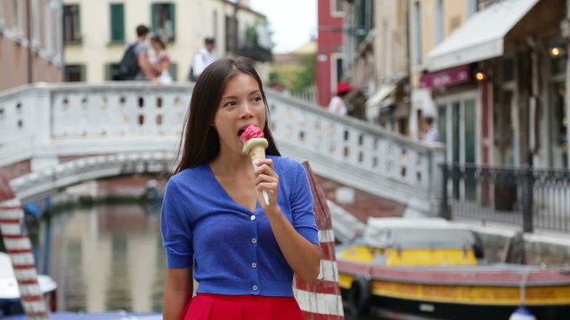 Woman in Venice, Italy eating Ice cream on vacation travel. Smiling happy Mixed race Asian Caucasian girl having fun eating italian gelato food outdoors during holidays in Venice, Italy, Europe.