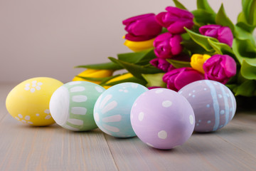 Easter painted eggs on wooden light background with spring bouquet tulips