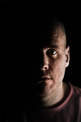 Fototapeta premium Adult Caucasian white man in deep shadows scruffy and unshaven looking at camera mysteriously while tired exhausted