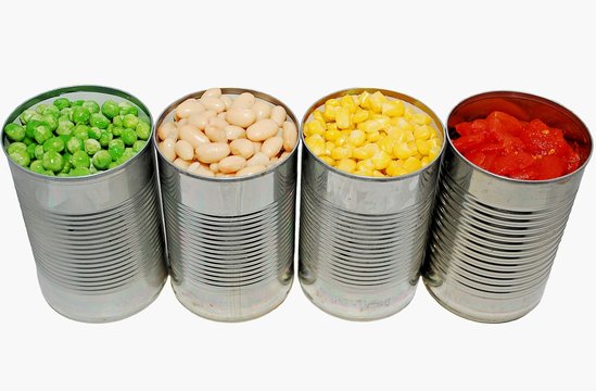 Opened cans of peas, cannellini beans, corn and tomatoes on a white background