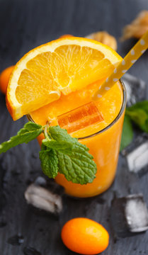 Orange smoothie in glass with yellow straw, fresh fruit slice, kumguat and perrepmint