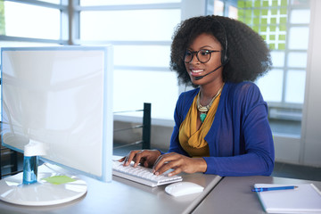 Portrait of a smiling customer service representative with an afro at the computer using headset - 103214804