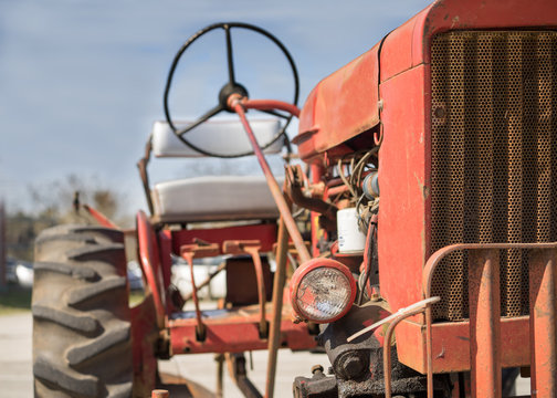 Old vintage antique red farm working tractor outside in the sun on a clear day 