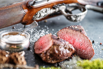 deer or venison steak with antique long gun and ingredients like sea salt and pepper, food background for restaurant or hunting loving - obrazy, fototapety, plakaty