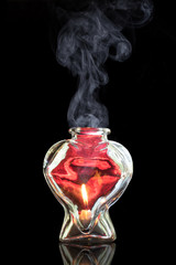 Smoke rising from red glass heart with fire flame inside representing romance potion love hope memory hardship connection anniversary dating valentines infatuation elixir danger emotion essence - 103216272