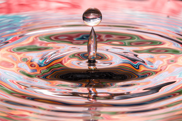 Single solitary drip drop splash of water into colorful reflective calm puddle pool creating...