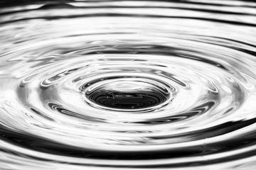 Single solitary drip drop of water into reflective calm puddle pool creating ripples waves rings...