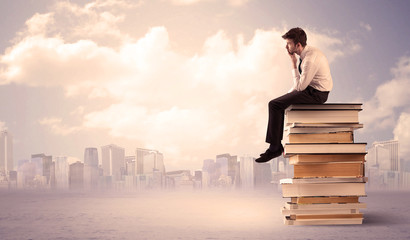 Man sitting on pile of books above city