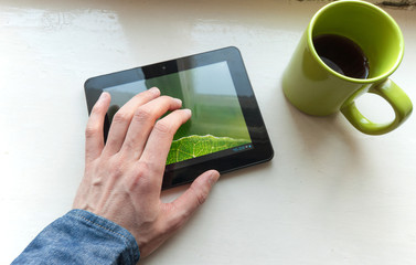 Young man drinking coffee in cafe and using tablet computer